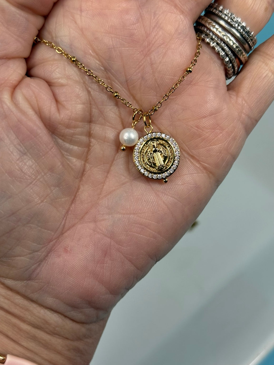 Detalle del dije de San Benito con circonias, acabado gold filled y perla
