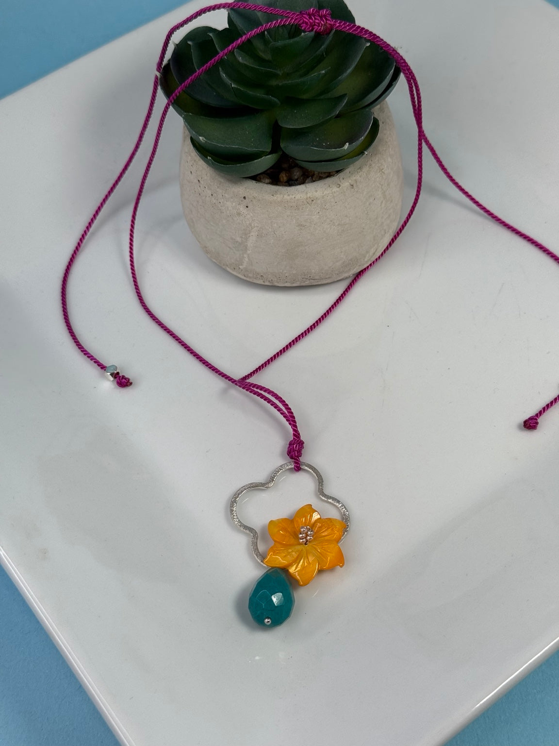Collar artesanal ajustable con flor de madreperla, jade azul turquesa y detalle enchapado en plata.