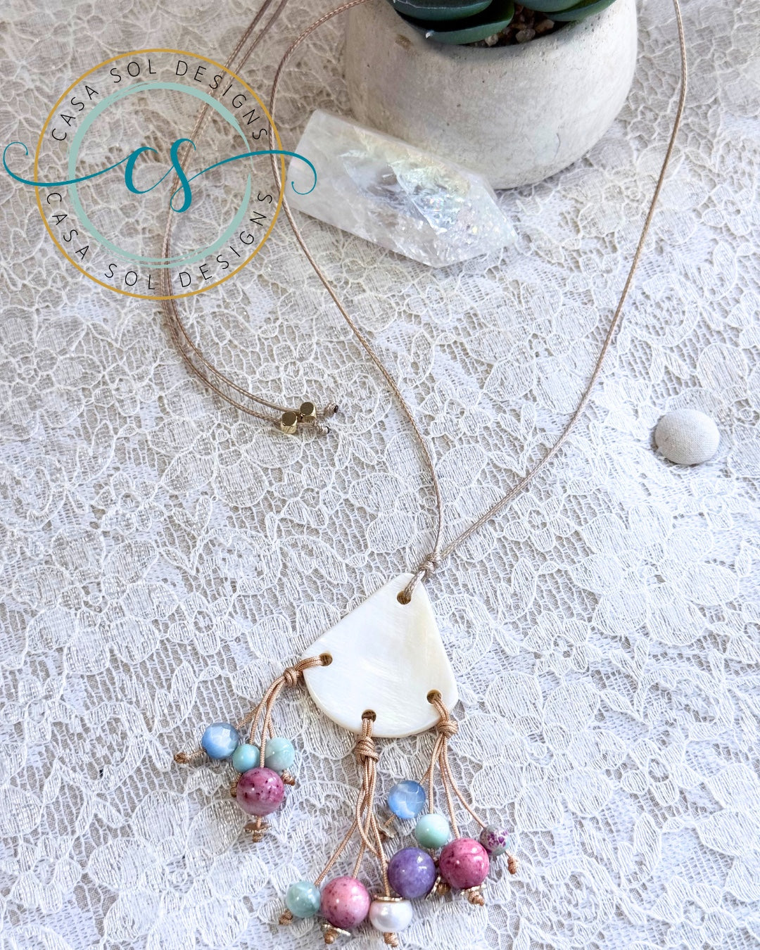 Collar ajustable de madreperla con jades de colores presentado sobre encaje.