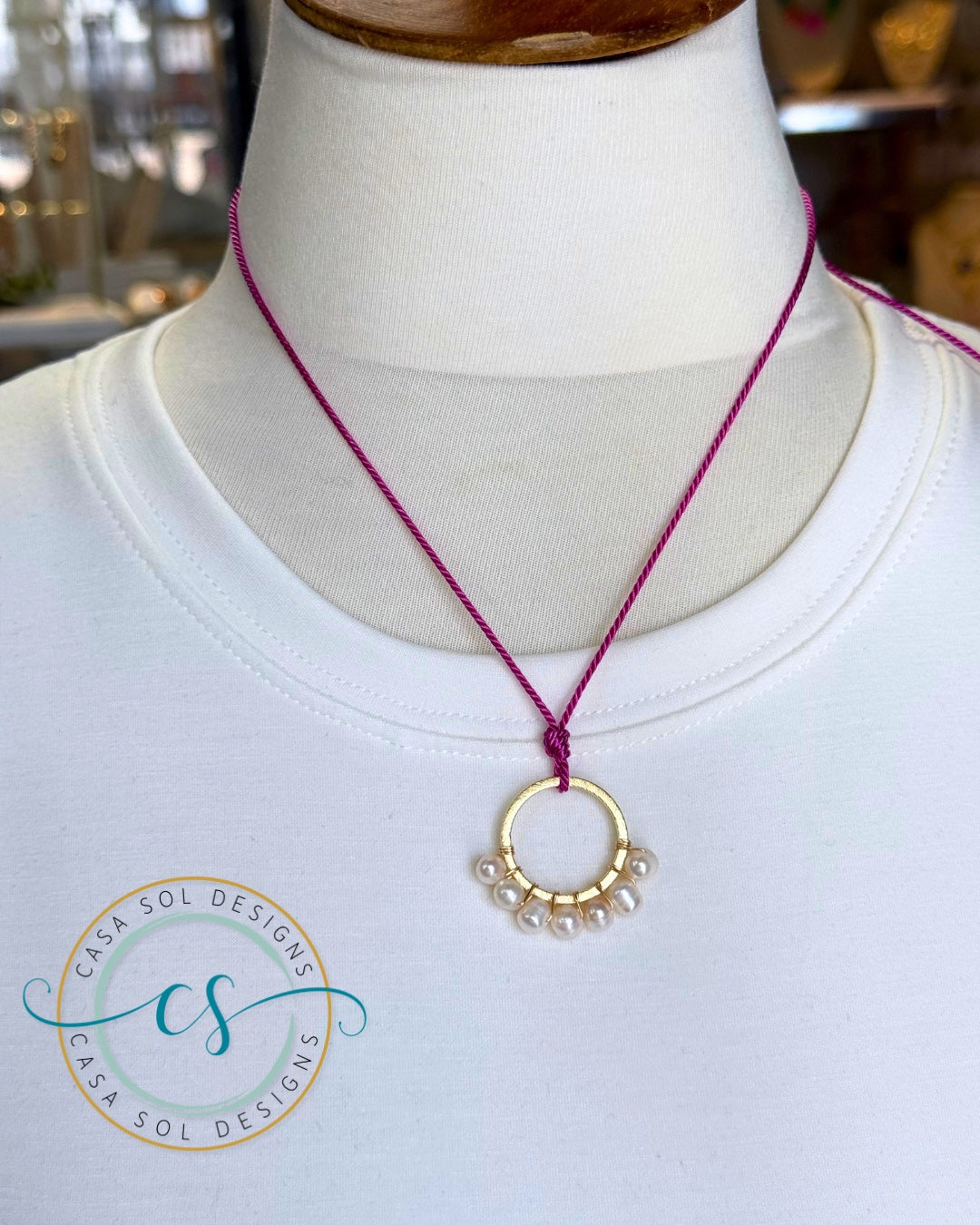 Collar artesanal en hilo frambuesa con perlas de agua dulce y aro dorado.