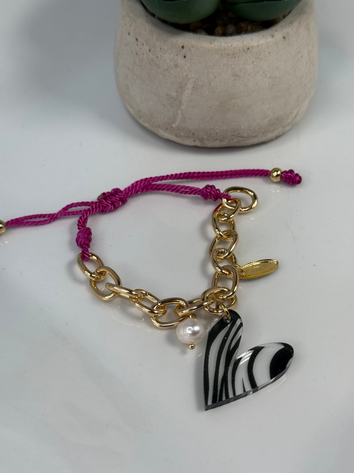 Detalle de pulsera ajustable con corazón rayado de acrílico y perla de agua dulce.