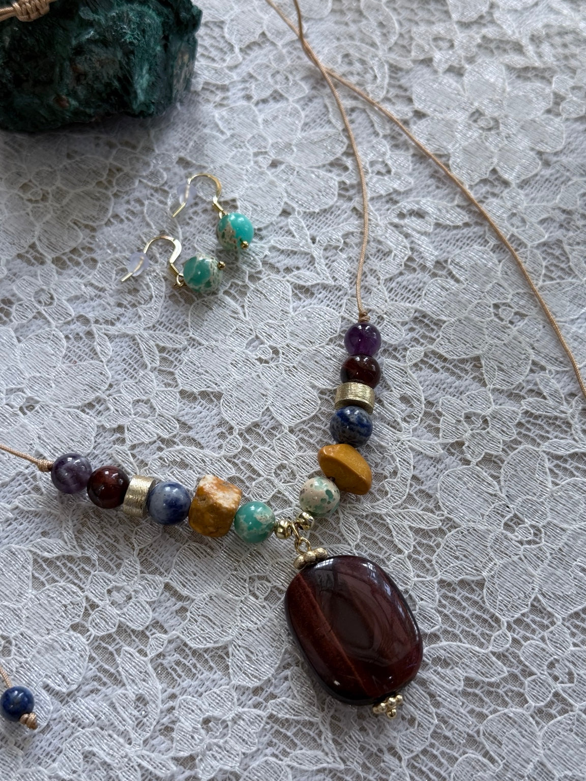 Set artesanal con collar ajustable y pantallas en piedras variadas y detalles dorados.