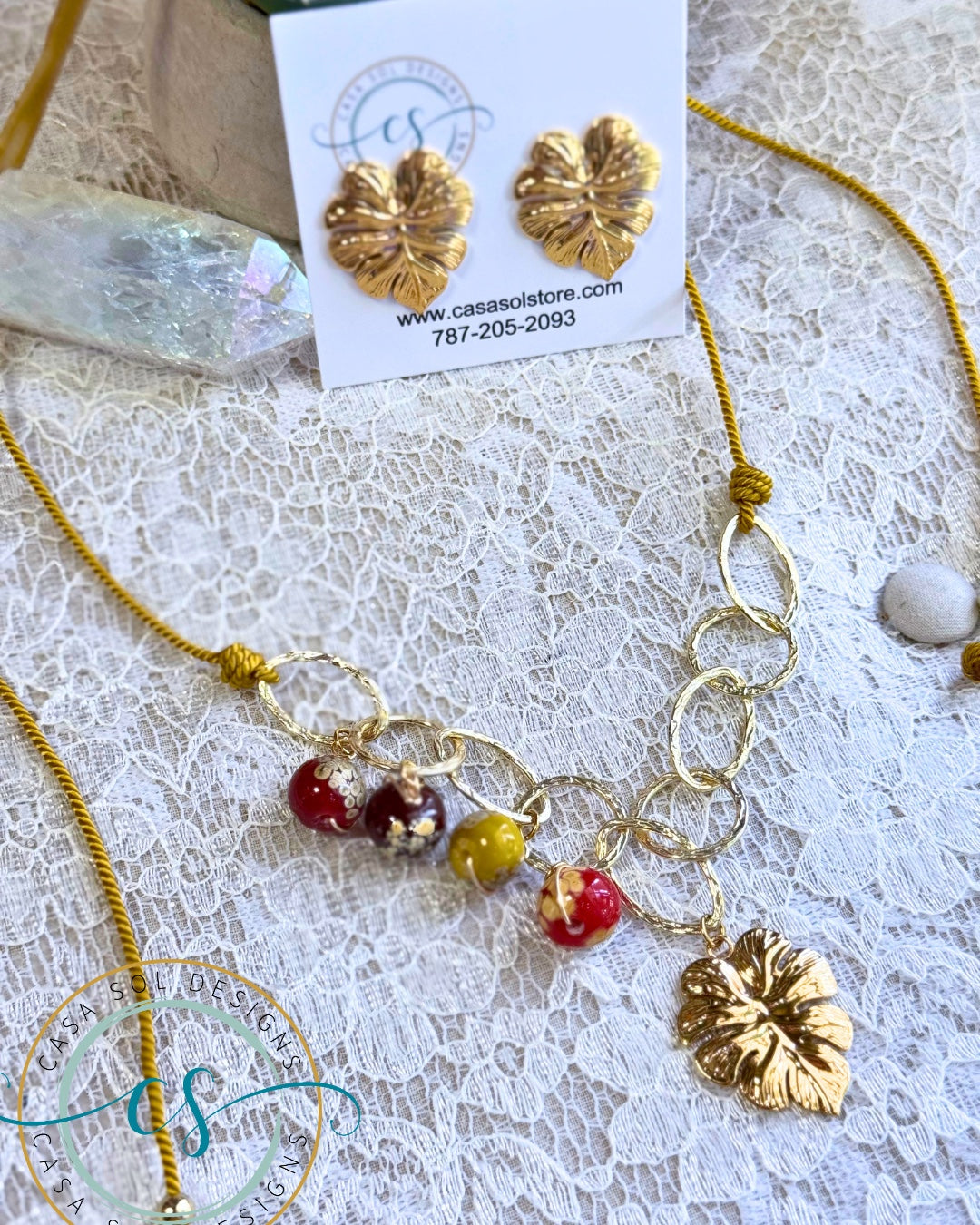 Set artesanal de collar ajustable con cristales de colores y hoja tropical acompañado de pantallas doradas.
